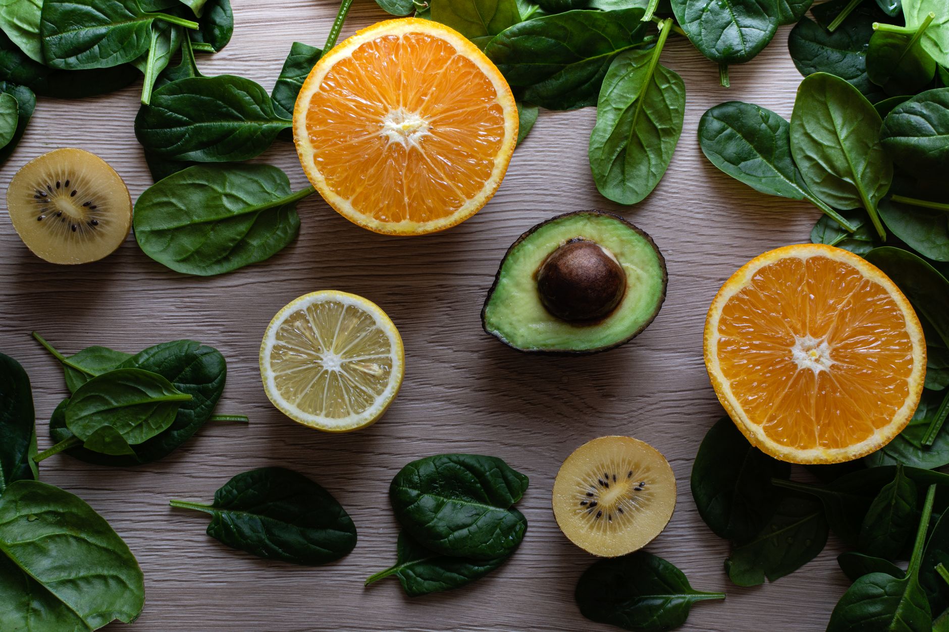 Alimentos ricos en folato: lentejas, espinaca, aguacate, naranja y brócoli sobre superficie de madera clara.