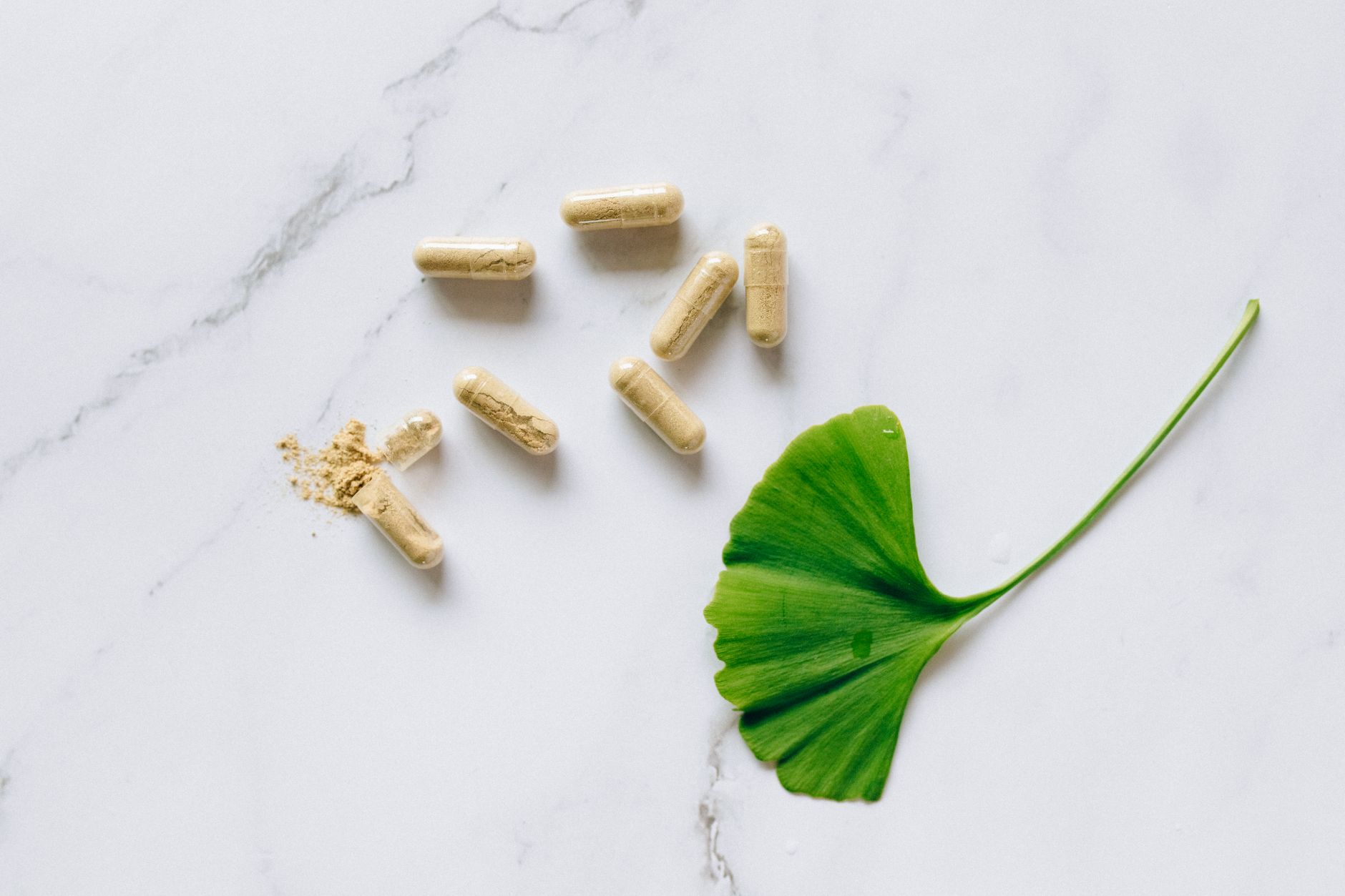 Vista superior de cápsulas de ginkgo biloba con una hoja sobre una superficie de mármol, que simboliza los suplementos naturales.