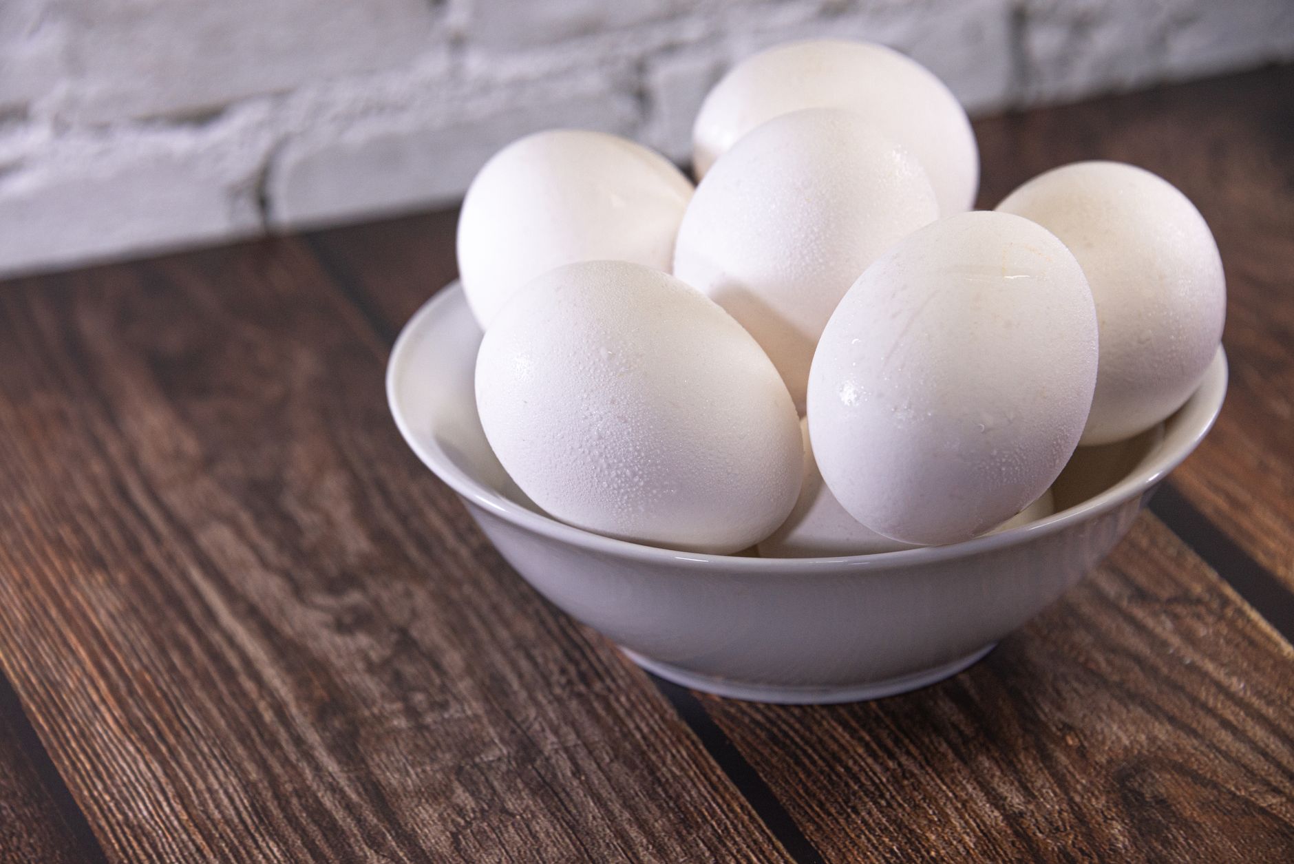 Huevos blancos frescos en un tazón de cerámica sobre una mesa de madera rústica.