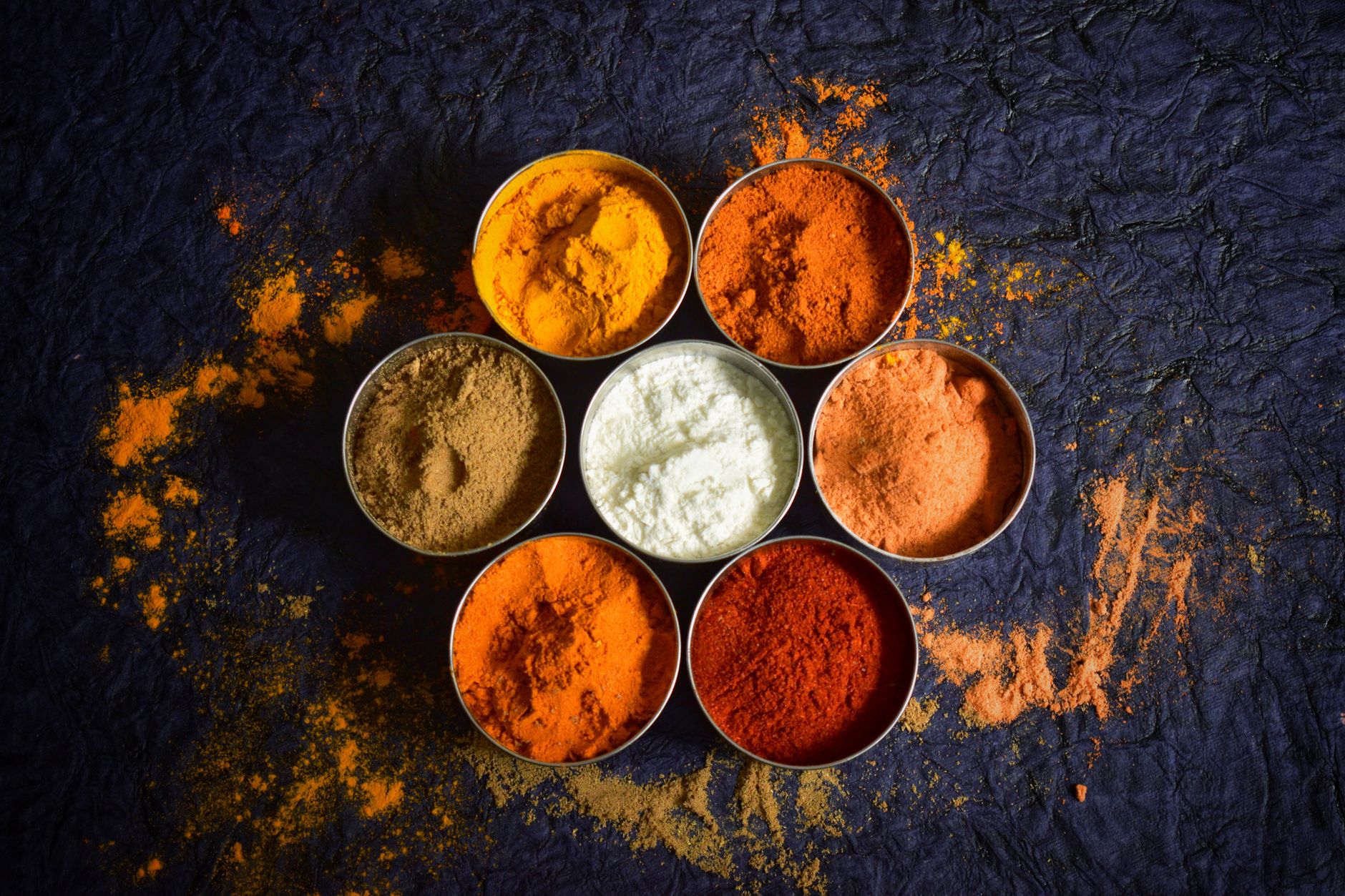 Especias indias coloridas en cuencos sobre un fondo oscuro con textura.
