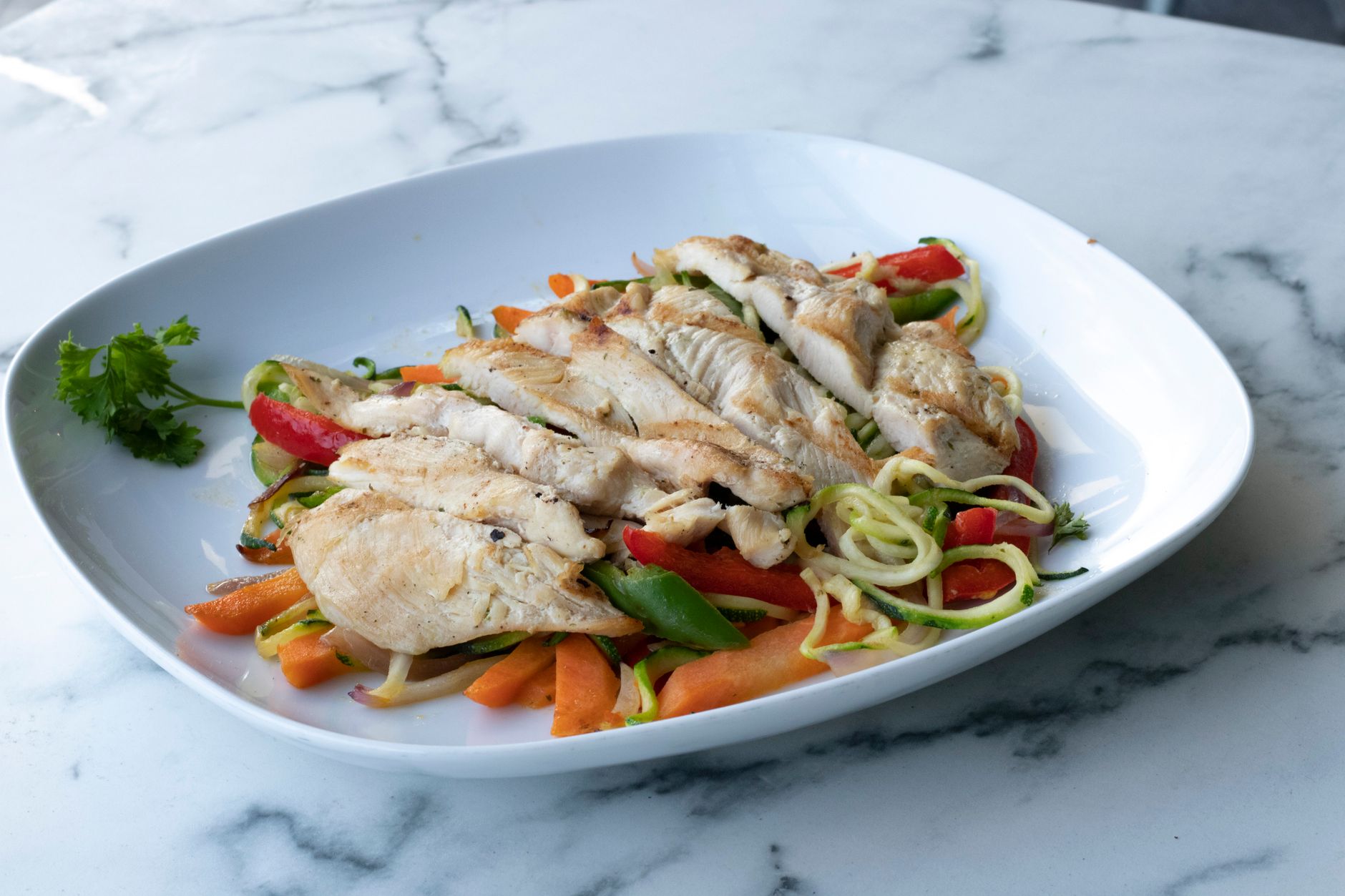 Pechuga de pollo a la parrilla servida sobre fideos de calabacín y verduras frescas.