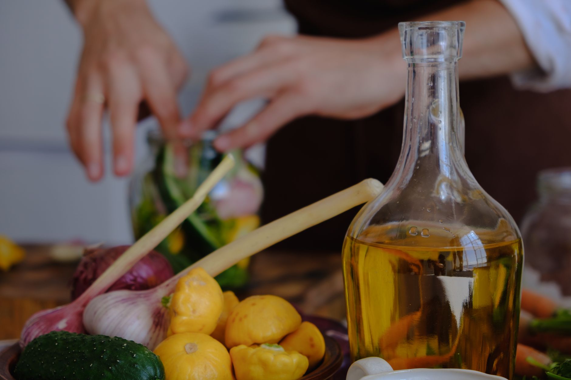 Manos preparando verduras con aceite de oliva, ajo y calabaza en una cocina.
