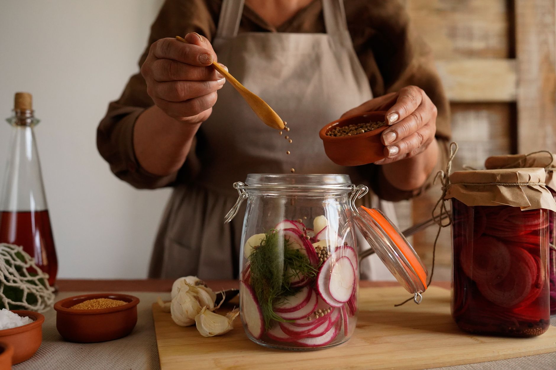 Manos preparando verduras en escabeche en un frasco, evocando un estilo de vida rústico y natural.