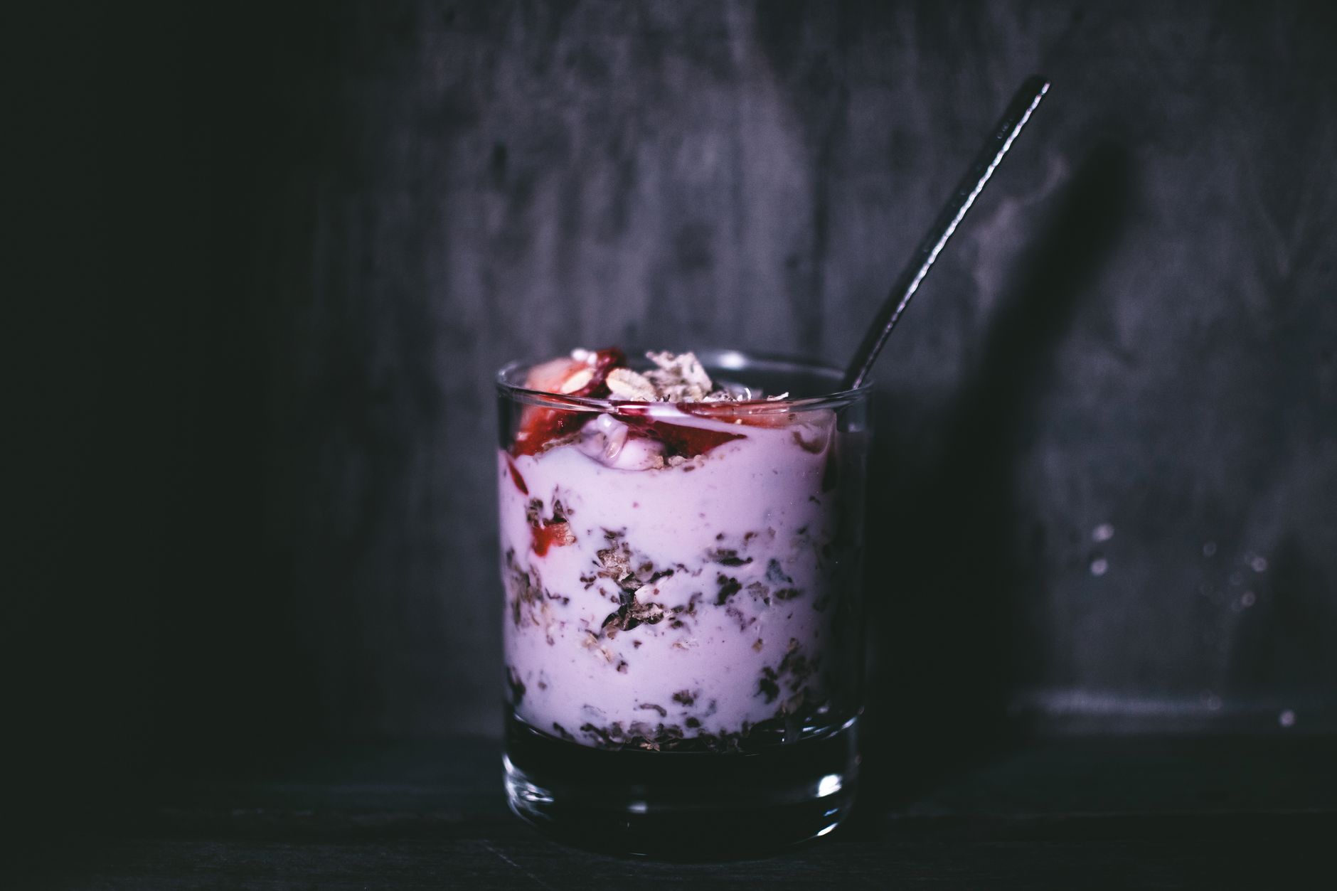 Primer plano oscuro y atmosférico de un delicioso parfait de yogur con granola y frutos rojos en un vaso.